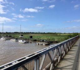view towards Walberswick across the Bailey Bridge at Southwold, with moored boats, then green meadows visible, on a sunny day