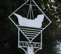 the white Dunwich village sign depicting an large old sailing ship enclosed within a square and with lines underneath to depict the sea
