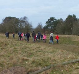 a group of people of various ages geocaching on a grassy path at Knettishall Heath
