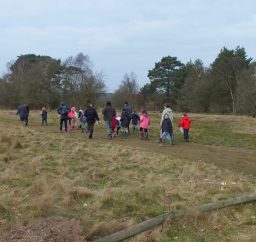Geocaching at Knettishall Heath a group of people of various ages geocaching on a grassy path at Knettishall Heath
