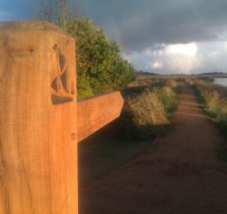 a wooden waymarker post along the Sailors' Path, bathed in orange sunlight with storm clouds in the distance