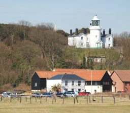 the white painted Lowestoft lighthouse on high ground overlooking buildings and the wooden structures used by fishermen to dry their nets