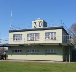 the Martlesham Control Tower Museum - a two-story pale green square building with a large 30 painted in black on a square structure on the roof, on a sunny day