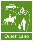 Green and white sign for Quiet Lanes, depicting an adult and child walking together, a person on a horse, a person on a bike, and a car