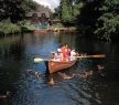 a family in a wooden rowing boat on the river, with trees on both sides at Flatford