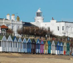 the large white painted Southwold lighthouse, with multi-coloured beach huts and the sandy beach in the foreground