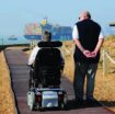 back view of a person in powered wheelchair with companion walking beside at Felixstowe Ferry