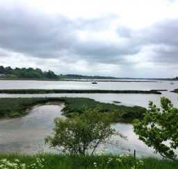 view across the River Deben from the river path at Woodbridge, with green spits of land and gently sloping green banks in the background, with a moody cloudy sky