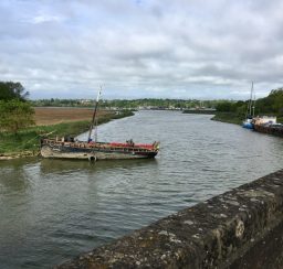 A view down the River Deben from Wilford Bridge, with two boats moored alongside the grassy banks